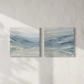 A pair of coastal paintings with blue, grey, white, cream, stone, teal, and yellow ochre paint hanging on a white wall by Teodora Guererra. 