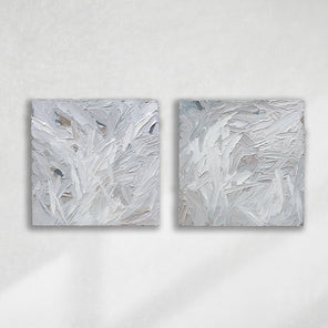 A pair of thickly textured paintings in grey, white, blue grey and plum grey by Teodora Guererra hanging on a white wall.