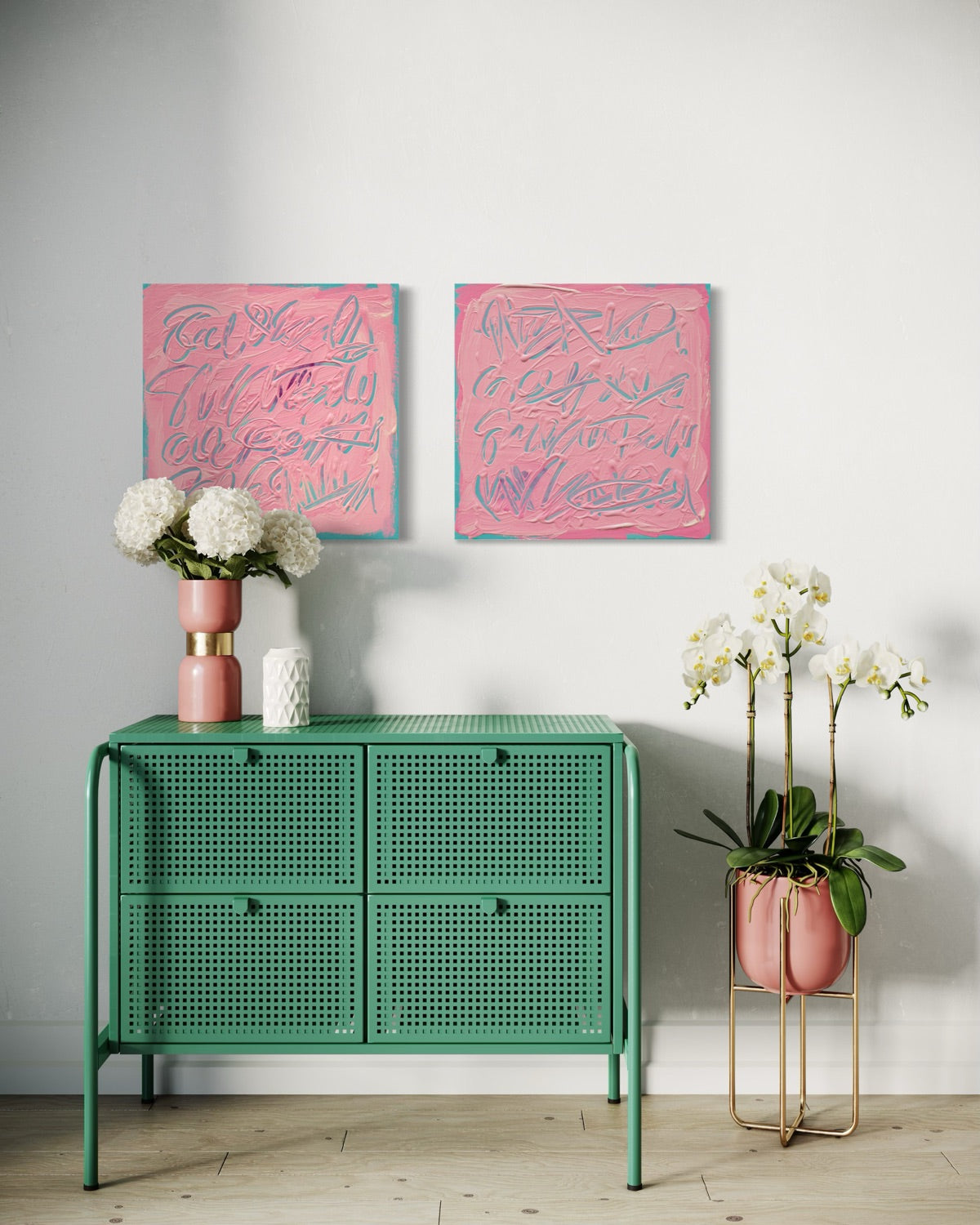 A styled interior scene showing two pink abstract wall art prints hanging above a mint green cabinet, with flowers and a potted orchid in a room with a white wall and light wood floor.