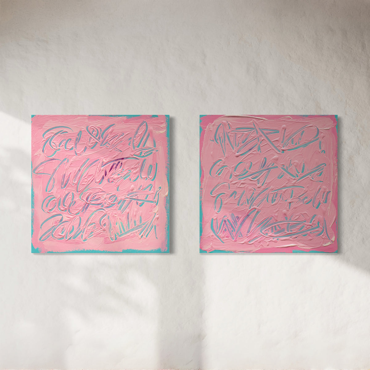 Two square pink text based paintings with writing into the surface with various tools, carving fluid script that reveals the teal color hidden below. Displayed side-by-side on a white wall with soft diagonal shadows.