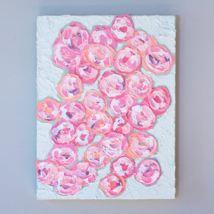 A very textured abstract painting with celadon background and circle type abstract flowers in pink, peach, plum and white hangs on a grey wall.