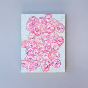 A very textured abstract painting with celadon background and circle type abstract flowers in pink, peach, plum and white hangs on a grey wall.