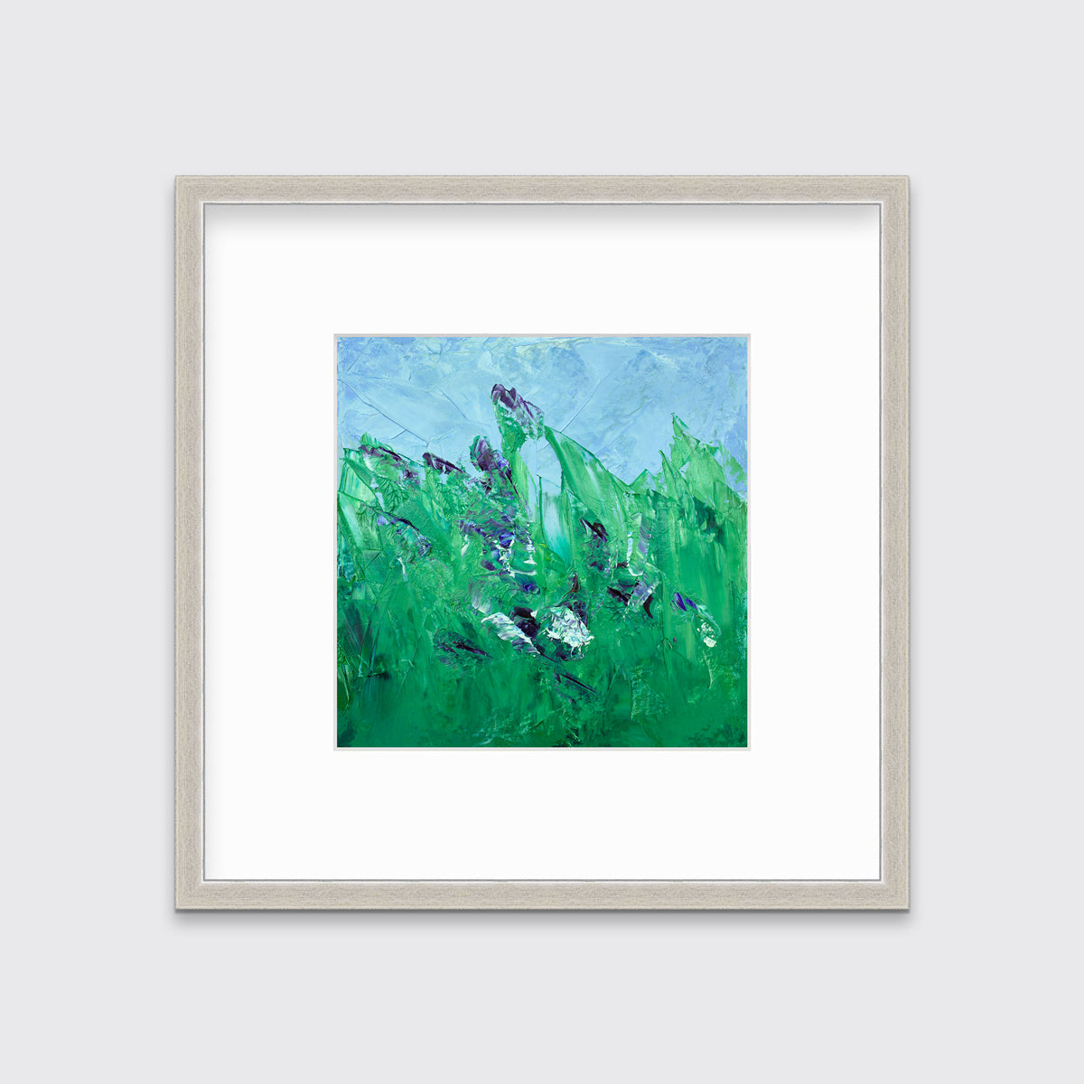 A blue and green abstract landscape print in a silver frame with a mat hangs on a white wall.