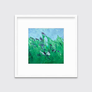 A blue and green abstract landscape print in a white frame with a mat hangs on a white wall.