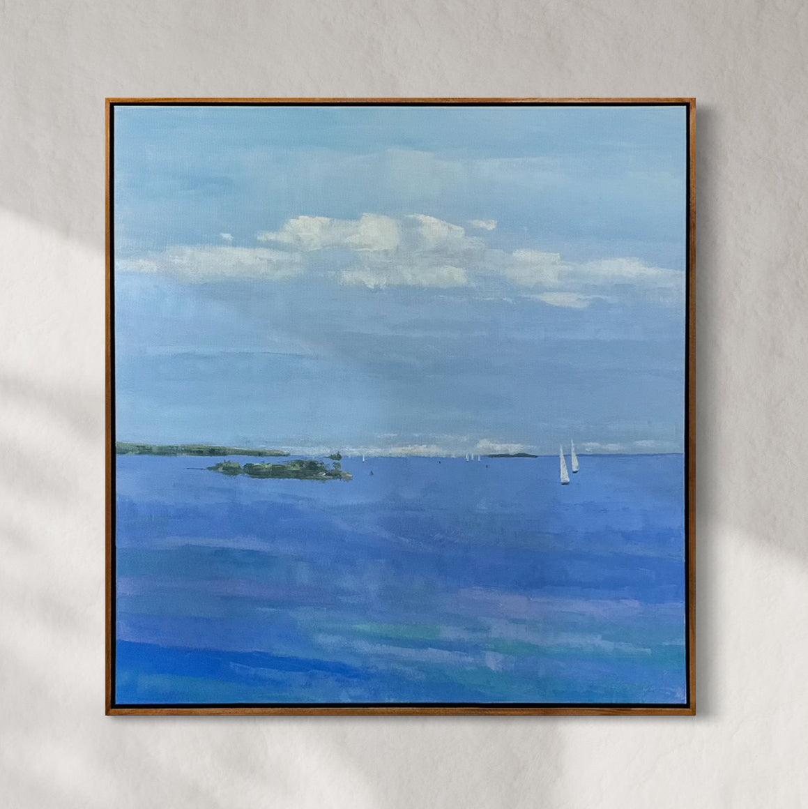Framed painting of a blue landscape with clouds and sailboats on a gray wall.