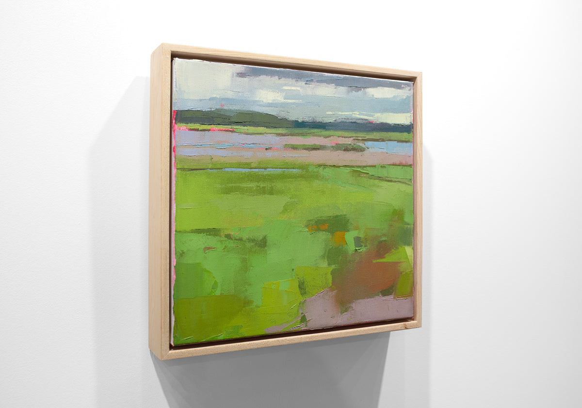 A blue and green framed textured abstracted landscape painting hangs on a white wall.