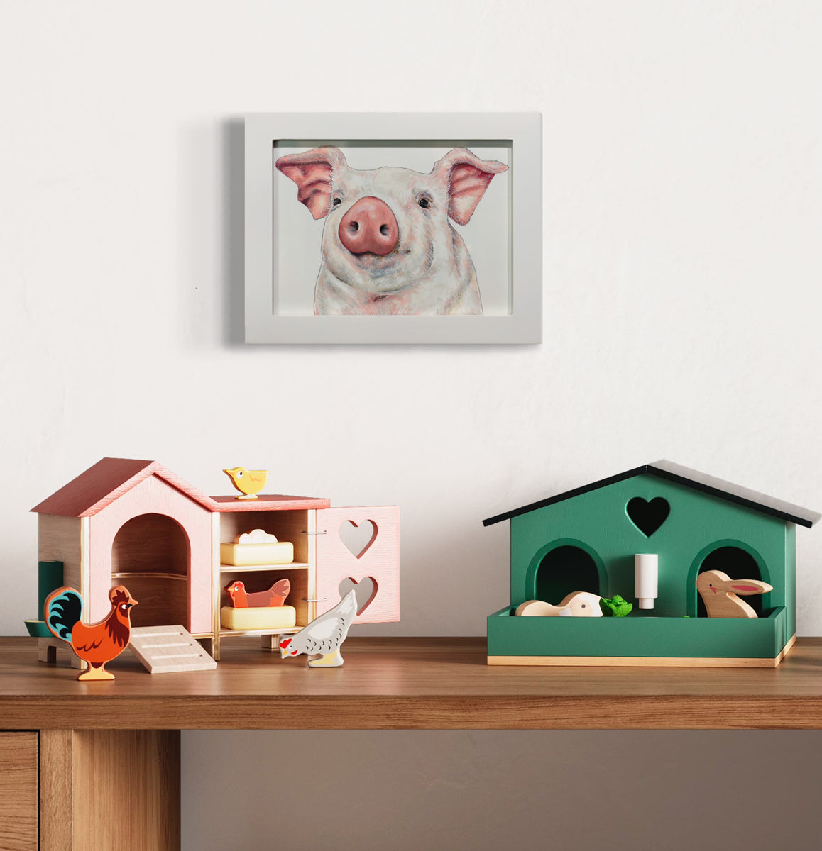 A framed illustration of a pig hangs on a white wall above a wooden desk with small pink and green wooden toys with bunny and chicken figurines.