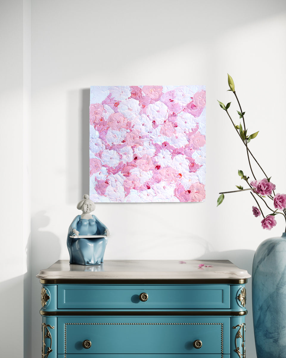 A very textured abstract painting with circle type abstract flowers in pink and white hangs on a white wall above a teal end table with a white marble top.