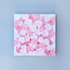 A very textured abstract painting with white background and circle type abstract flowers in pink and white hangs on a grey wall.