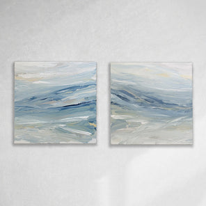 A pair of coastal paintings with blue, grey, white, cream, stone, teal, and yellow ochre paint hanging on a white wall by Teodora Guererra. 