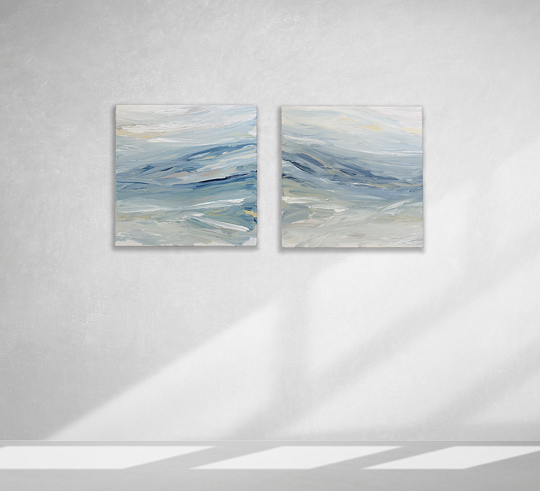 A pair of coastal paintings with blue, grey, white, cream, stone, teal, and yellow ochre paint hanging on a white wall by Teodora Guererra.