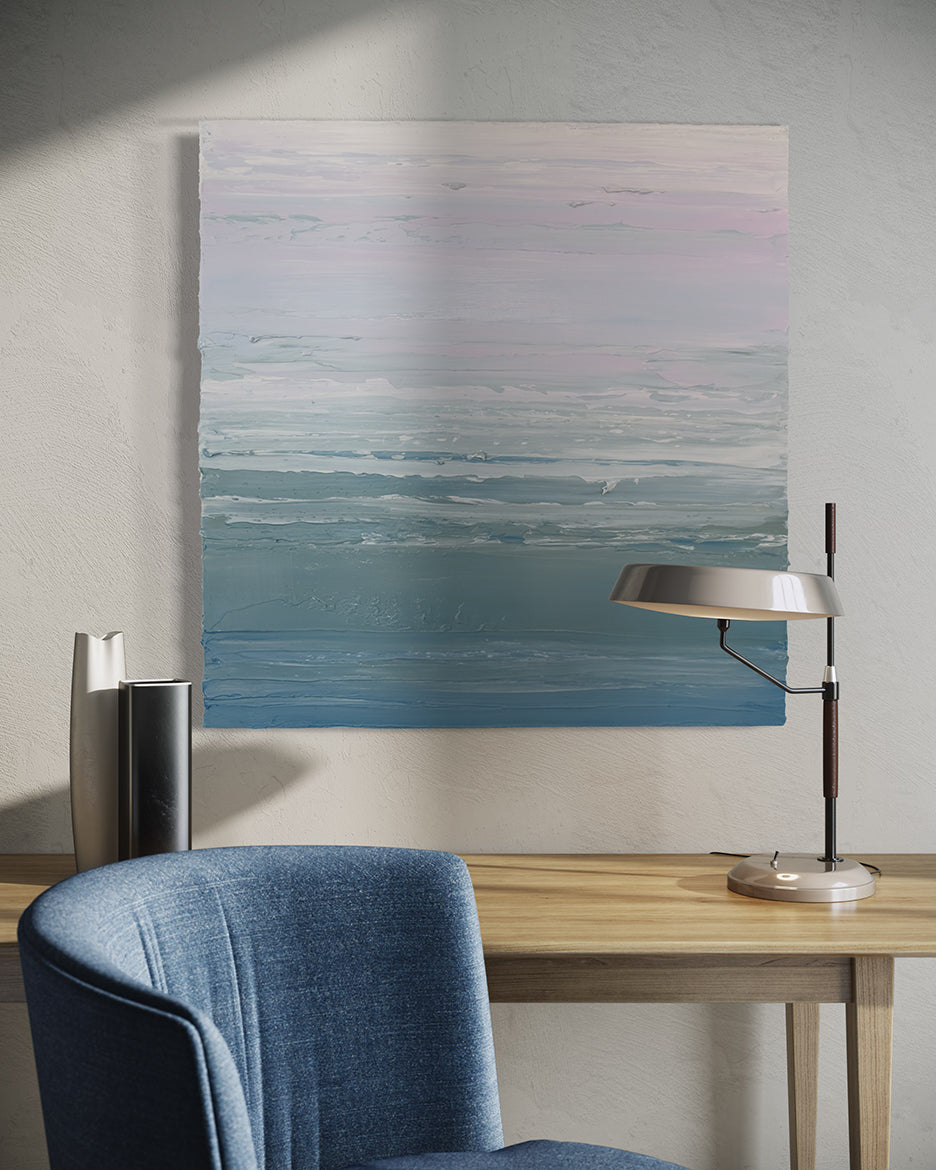 A teal blue, teal green, lavender and pale lavender textured abstract painting by Teodora Guererra hangs on a white wall. above a maple table with a lamp and 2 decorative vases. A blue chair sits in front.