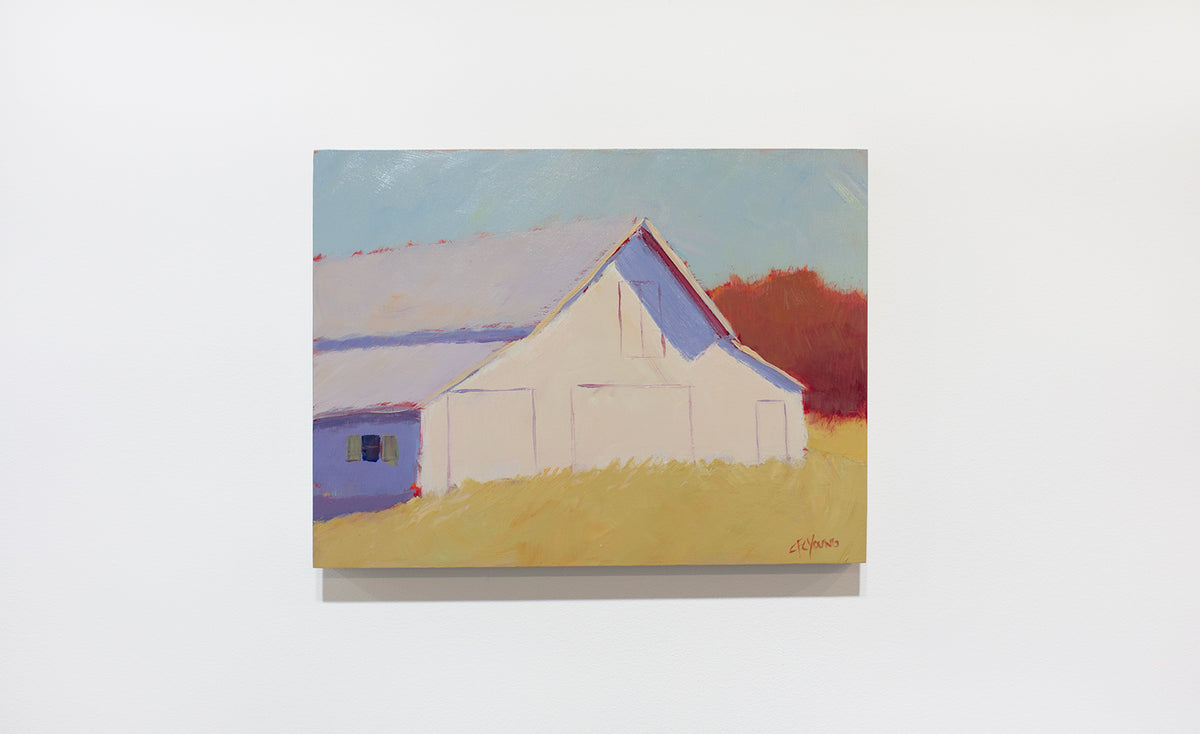 A landscape painting of a barn in a field hangs on a white wall. 