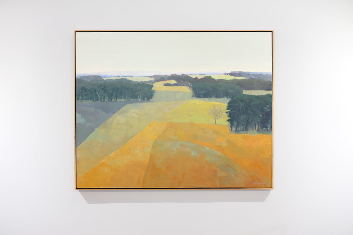 A framed yellow and green abstracted landscape painting hangs on a white wall. 
