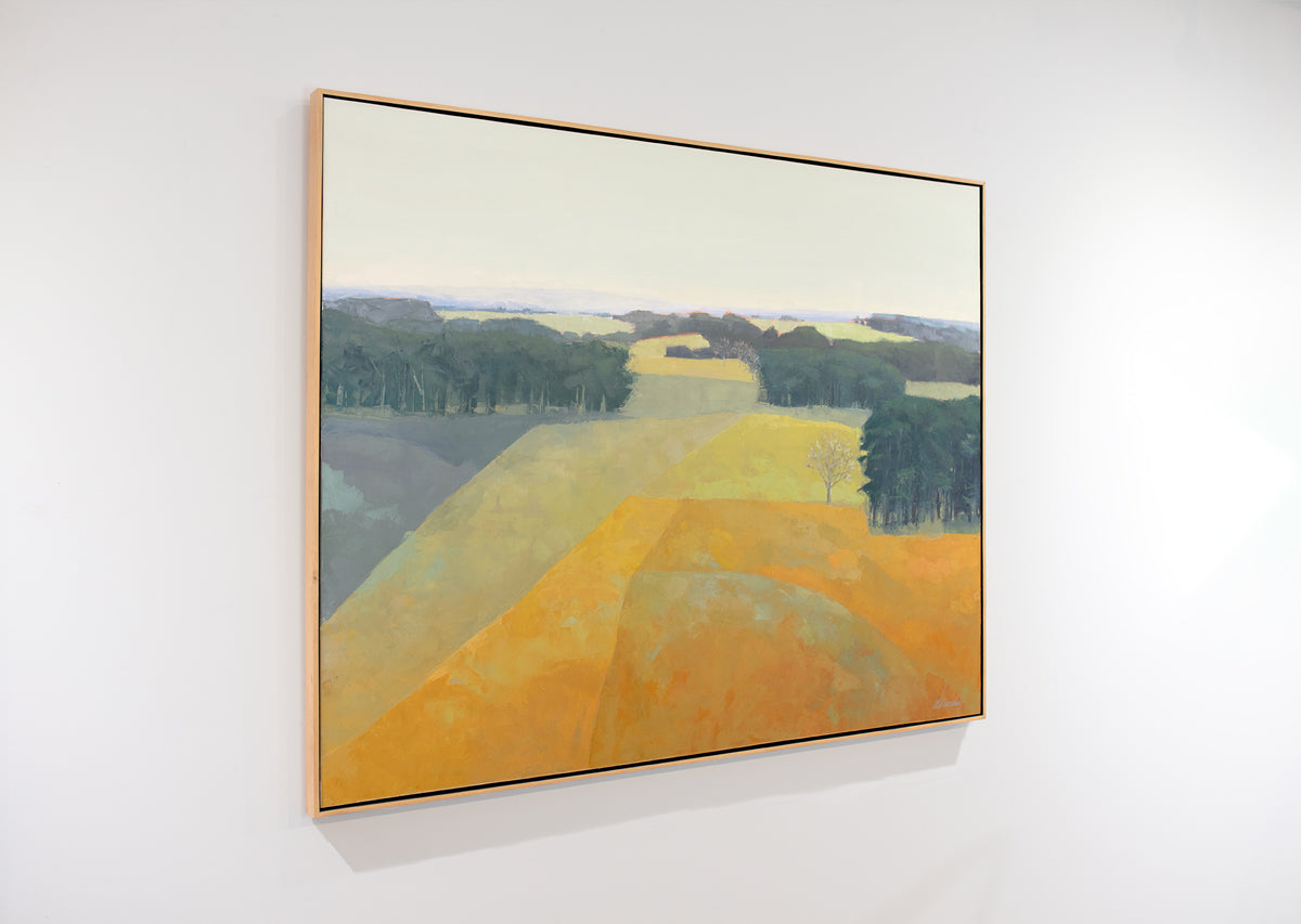 A framed yellow and green abstracted landscape painting hangs on a white wall.