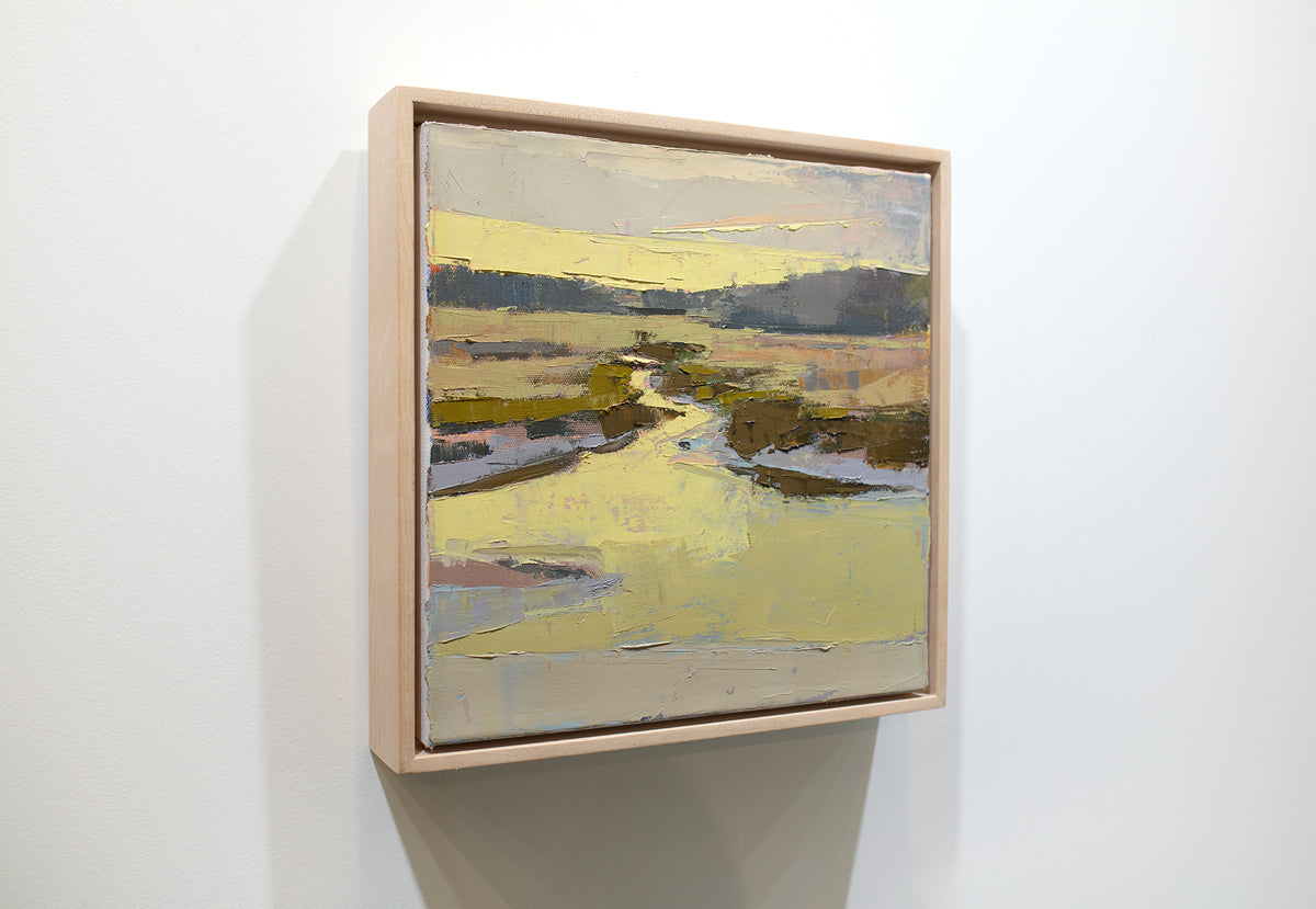 A framed yellow and brown abstracted landscape painting hangs on a white wall.