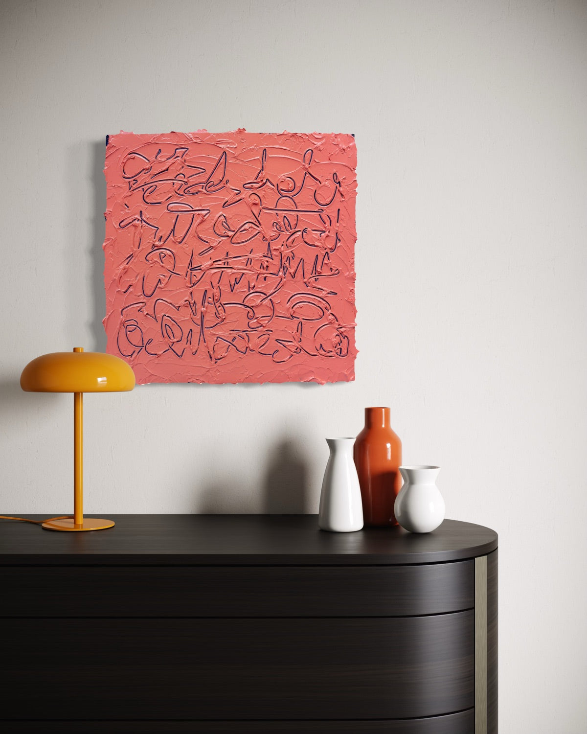 A square abstract painting with textured coral-pink background and dark scribbled line work, displayed on a light gray wall above a dark wooden console table with a yellow lamp and ceramic vases.