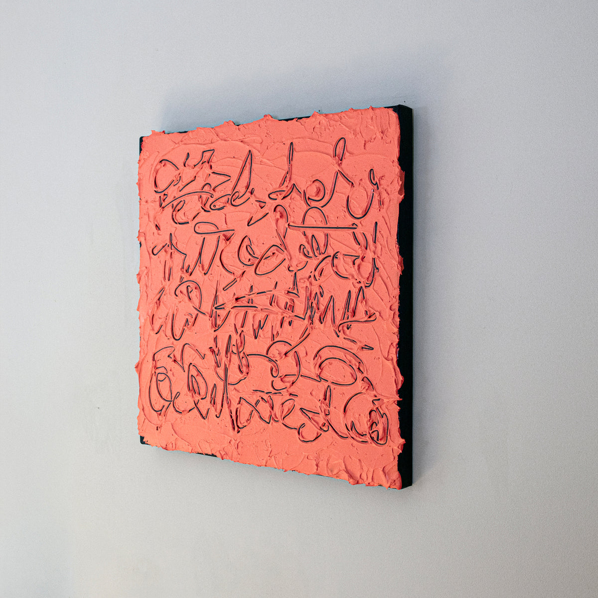 A square abstract painting with a textured coral-pink surface and dark calligraphic line work, mounted against a light gray wall.