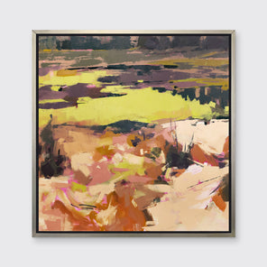 A yellow and orange abstracted landscape art print framed in a silver frame hangs on a white wall. 