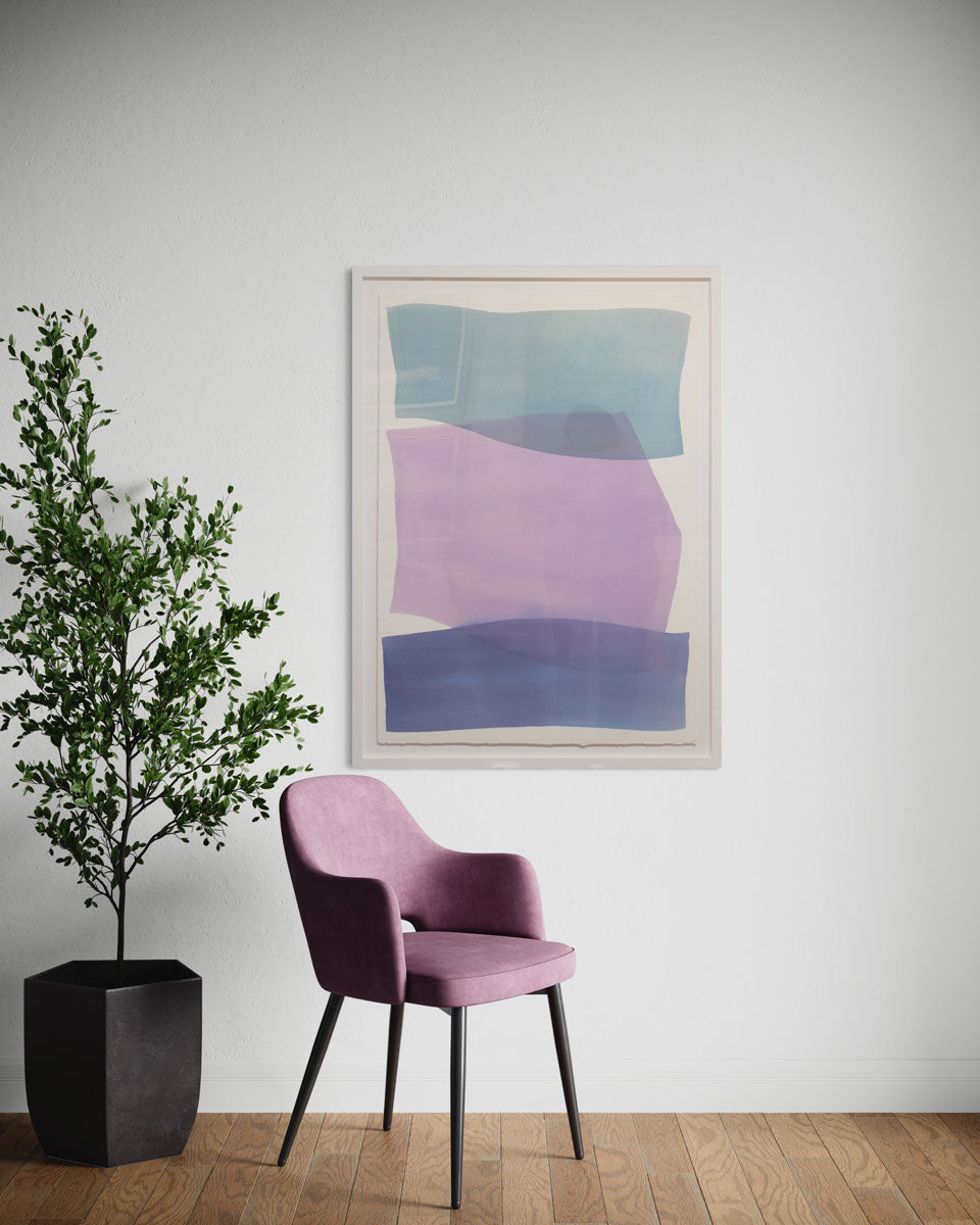 A framed blue and violet abstract painting hangs on a white wall above a muted pink chair and potted floor plant. 
