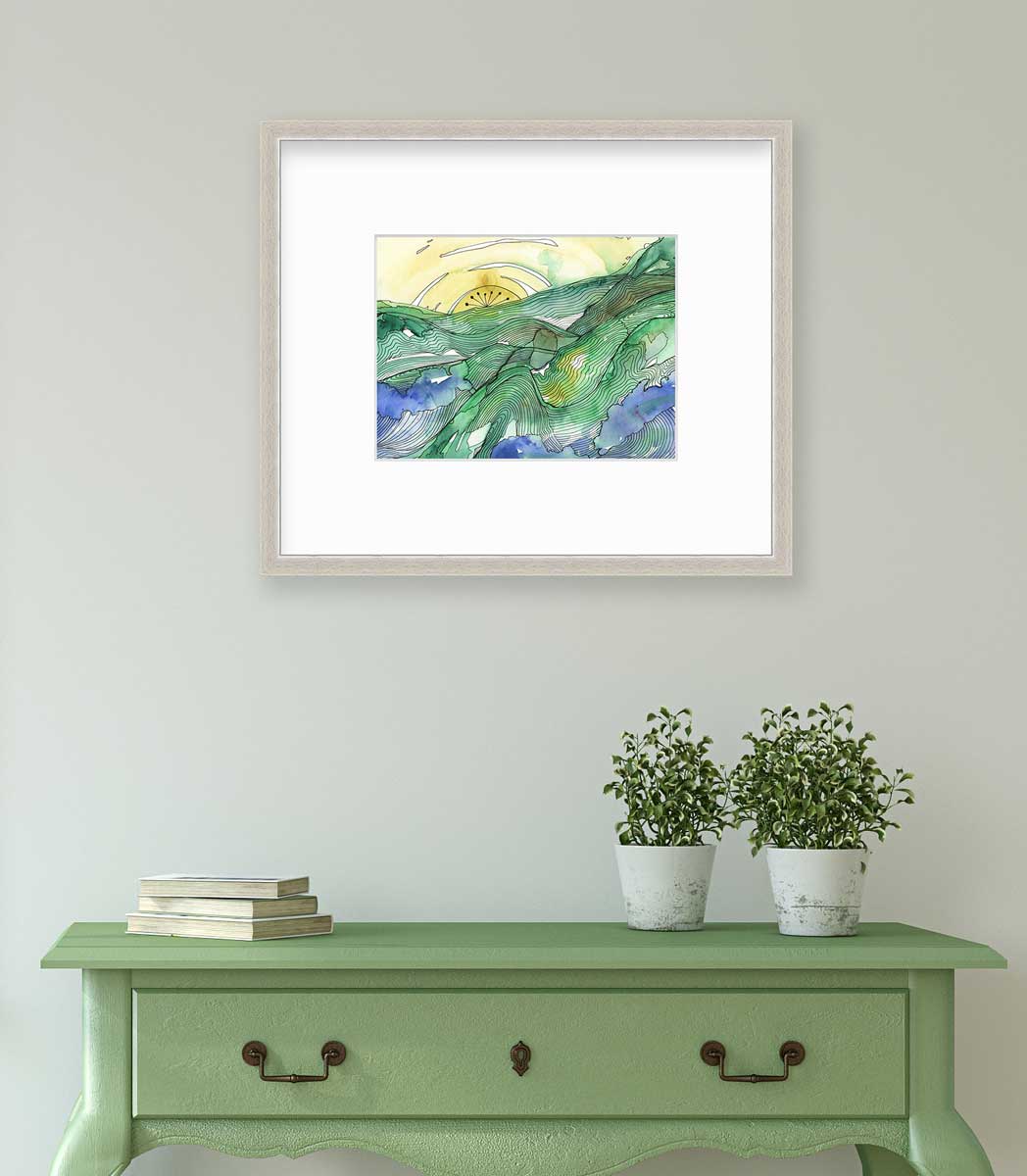 A yellow and green landscape illustration print framed in a silver frame with a mat hangs on a white wall above a green console table with a stack of books and two potted plants.