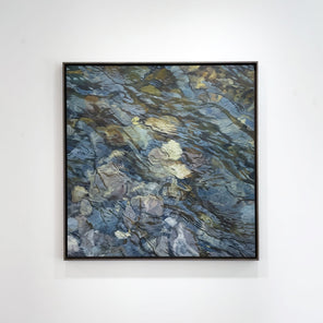 An oil painting of river rocks hangs on a white wall. 