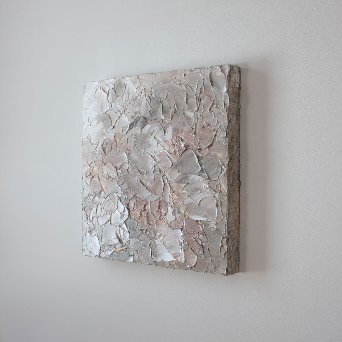 A painting is shown hanging on the wall at an angle. Its surface is decorated with white, pink and grey paint in a thick impasto. Wired and ready to hang.