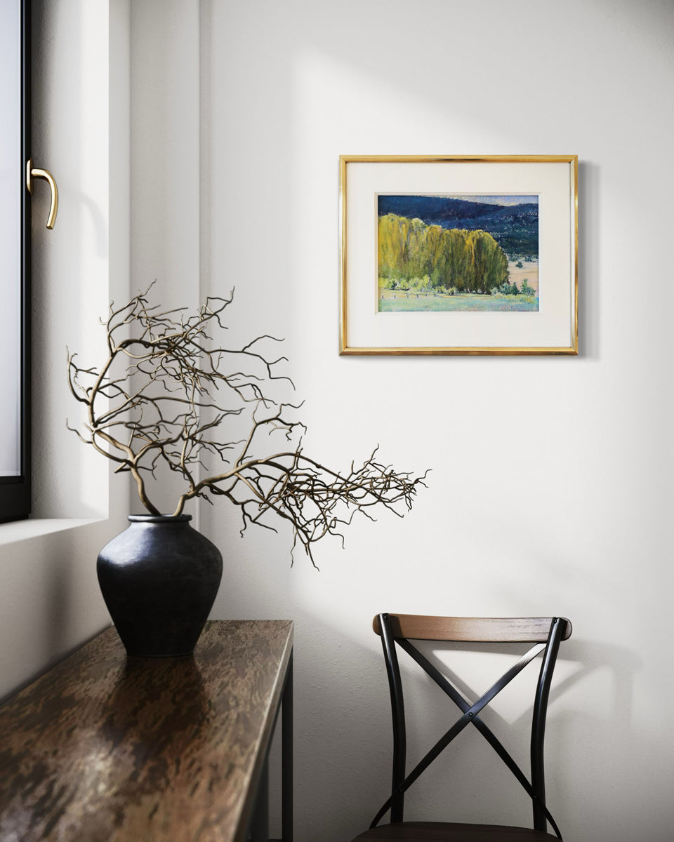 The painting, Study, Highland Greens by Ken Elliott matted in a gold frame hanging on a white wall above a chair by a window.