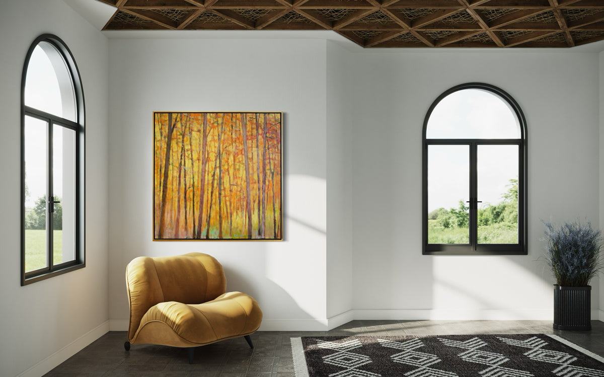 An impressionistic painting similar to Wolf Kahn with tall brown trees with orange and red leaves and a warm yellow background. The painting hangs in a room over a yellow chair.
