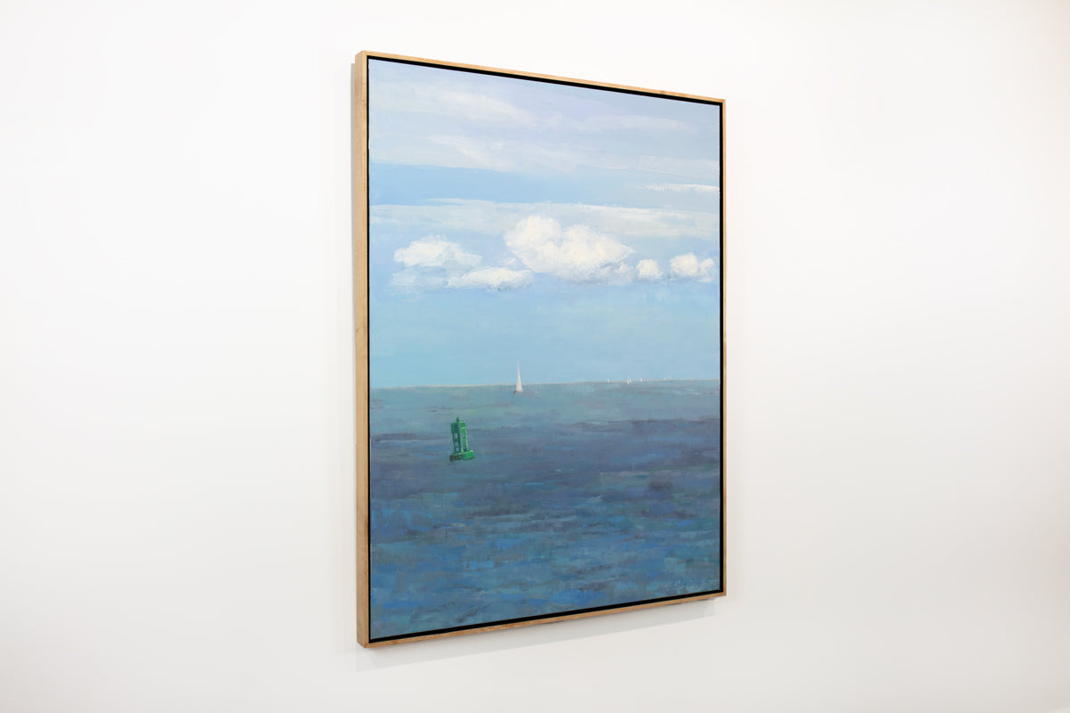 A side view of a blue, white and green coastal landscape painting by Molly Doe Wensberg hangs in a light wood floater frame on a white wall.