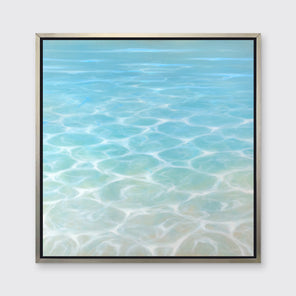 A tonal teal, white and beige abstract seascape print in a silver floater frame hangs on a white wall.