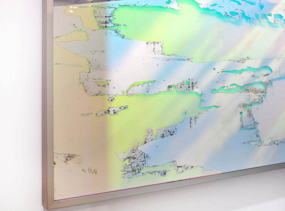 A detail of a fine art mirror framed in a champagne-toned frame hanging on a white wall. 