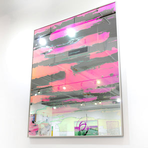 A pink fine art mirror hangs on a white wall in an art gallery. 