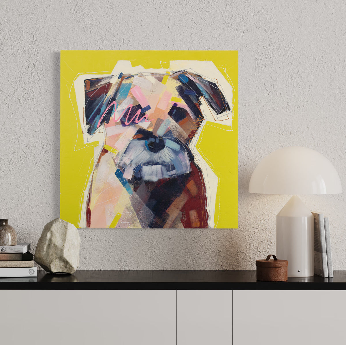 A bright yellow painting of an abstracted dog hangs on a textured white wall above a black and white console table with modern table decor and books. 