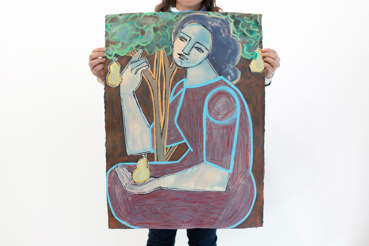 A woman holds an abstracted painting on paper of a woman embracing a tree and holding a pear in her left hand in front of a white wall. 