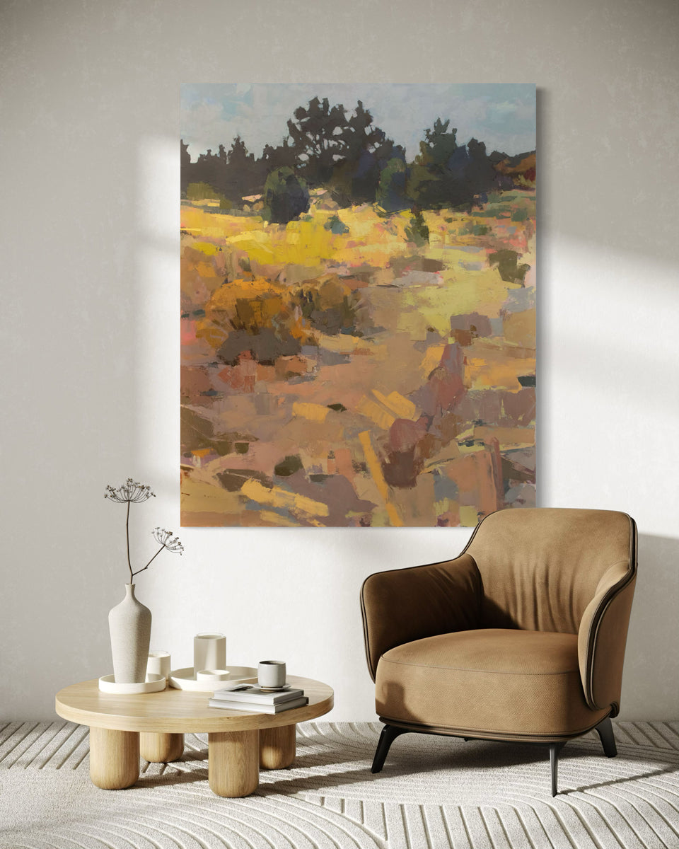 An abstracted landscape painting hangs on a white wall above a camel colored chair.