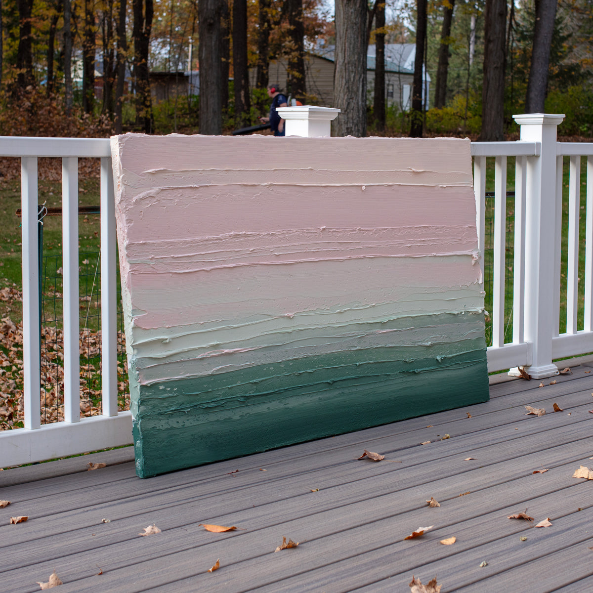 A light Coral, light pink, celadon and hunter green thickly textured abstract painting by Teodora Guererra leaning outside on a deck.