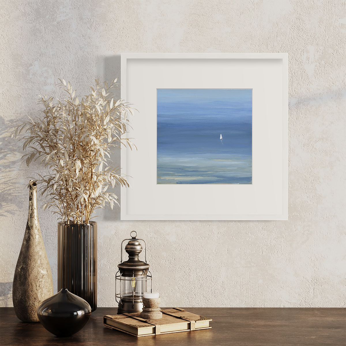 A blue, light green and white abstract seascape print with a small sailboat in a white frame with a mat hangs on a white wall above a wood surface with vases, a book and a small lantern.