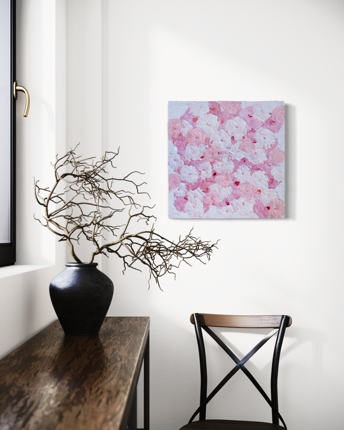 A very textured abstract painting with circle type abstract flowers in pink and white hangs on a white wall above a chair, A console sits to the left with a pot of dried decorative branches.