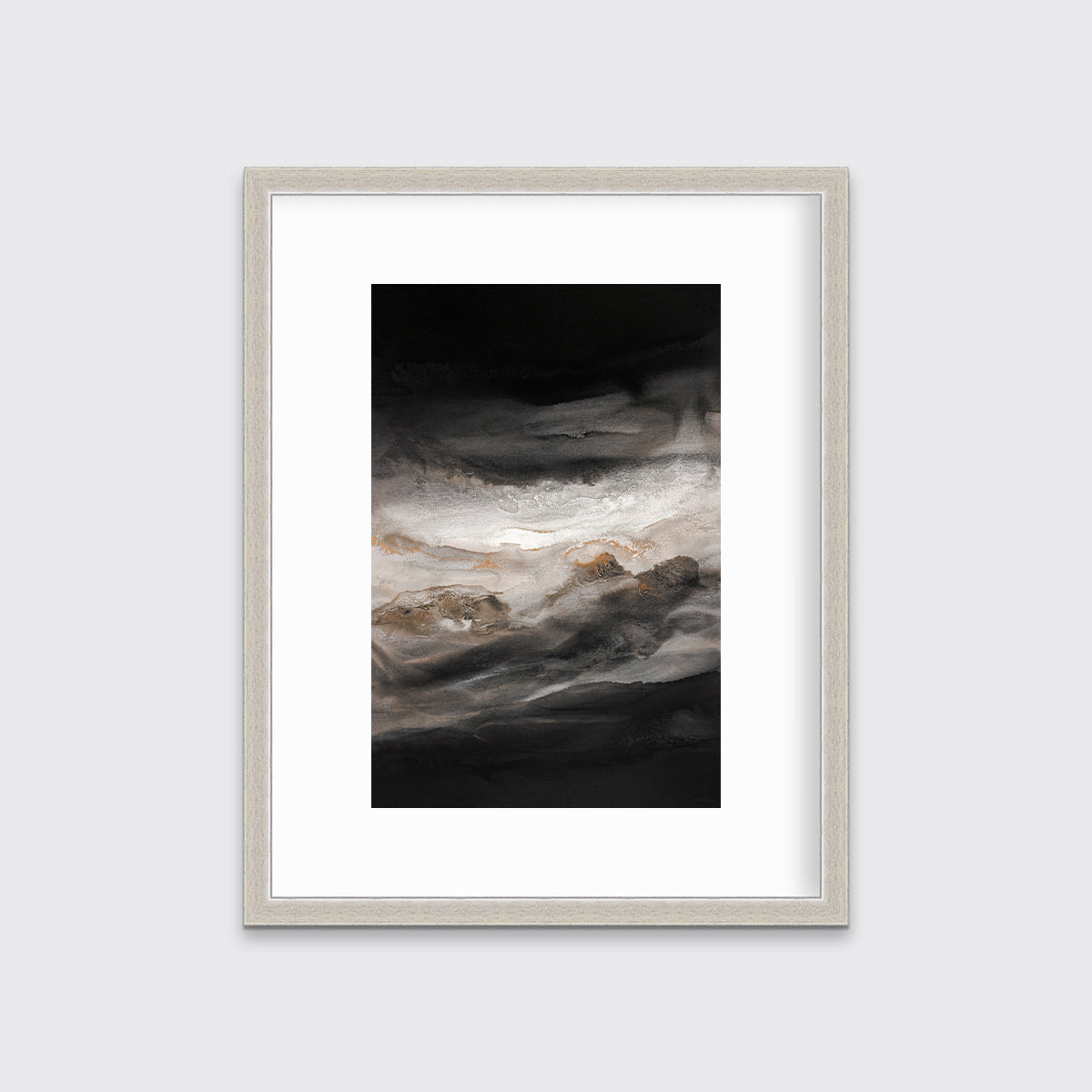 A black, white, beige and gold abstract print in a silver frame with a mat hangs on a white wall.