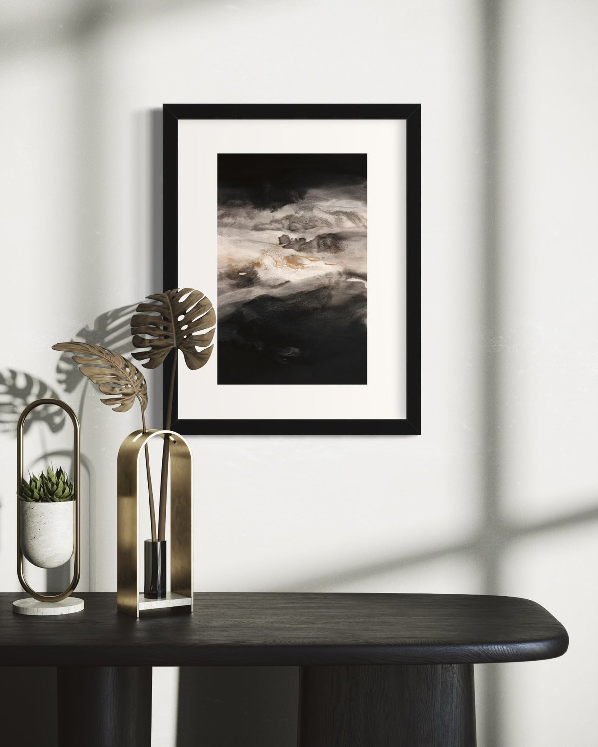 A black, white, gold abstract print framed in a white mat and black frame hangs on a wall over a black credenza with decorative objects.