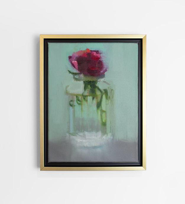 A small framed painting of a red flower in a clear glass vase, framed in a gold floating frame, hangs on a white wall.