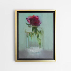 A small framed painting of a red flower in a clear glass vase, framed in a gold floating frame, hangs on a white wall.