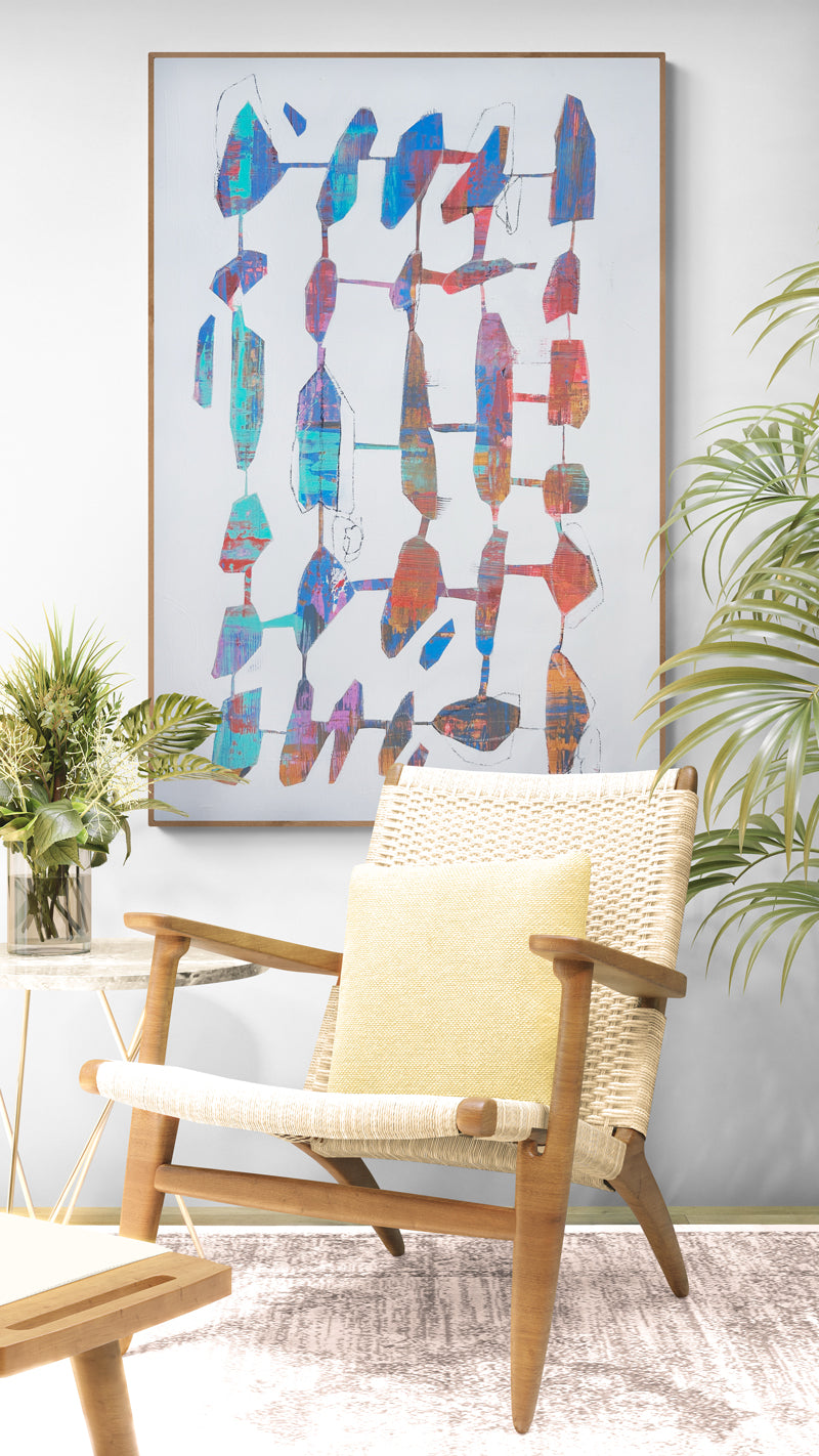 Colorful abstract painting on a wall above a wicker chair with a yellow cushion.