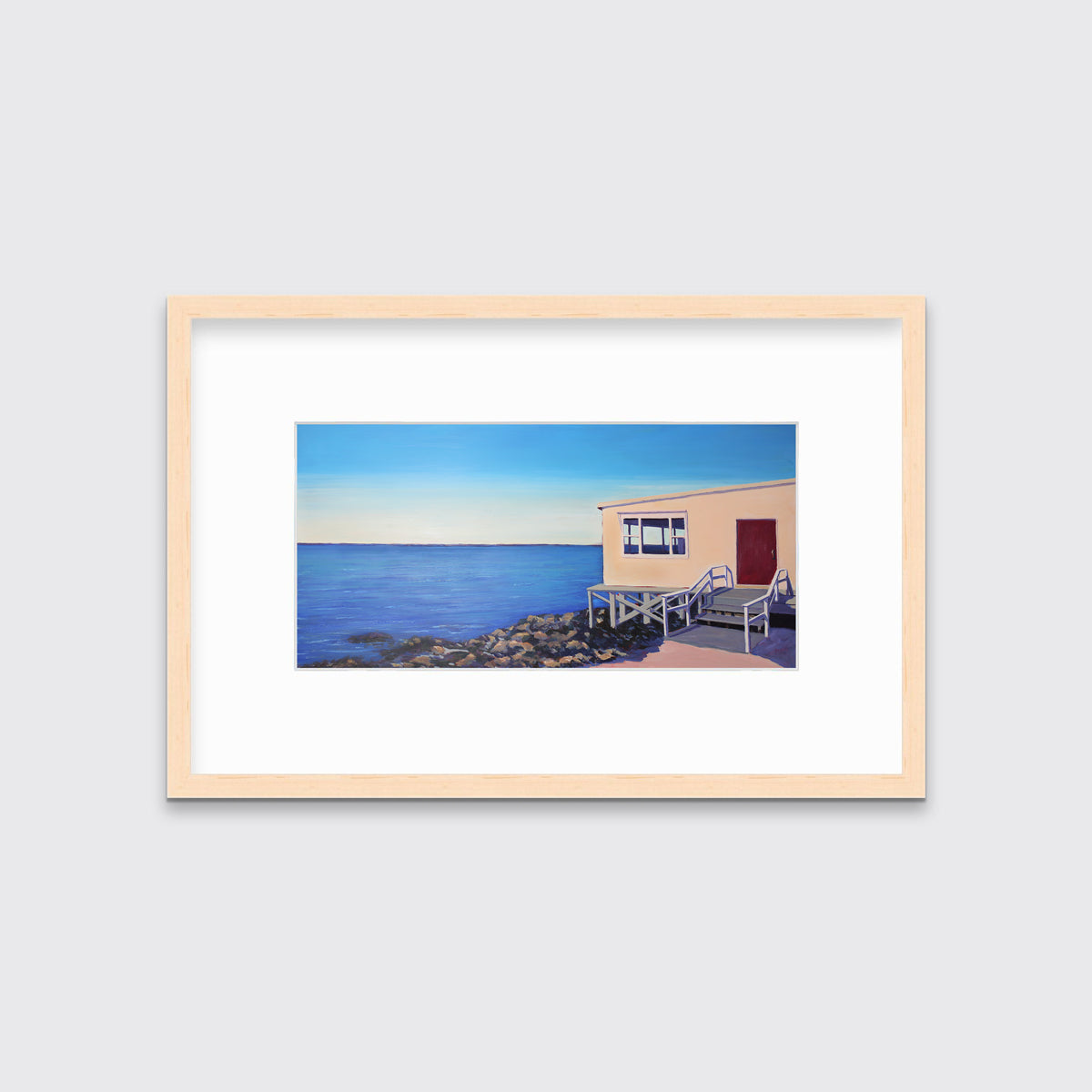 A contemporary seascape print in a natural wood frame with a mat hangs on a white wall.