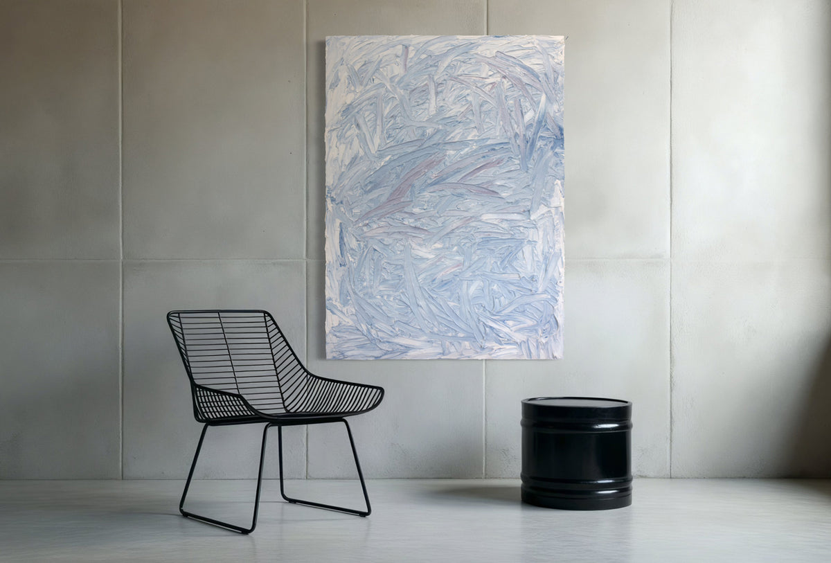Abstract painting on a wall above a wire chair and black cylindrical object.