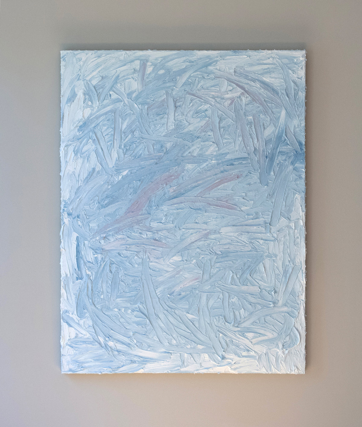 A blue and white textured painting hangs on a grey wall in the artists studio.