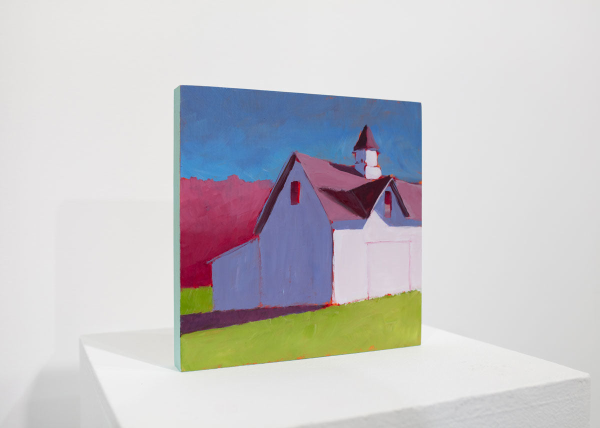 A pink, blue, and green contemporary landscape painting sits upright on a white table surface in front of a white wall.