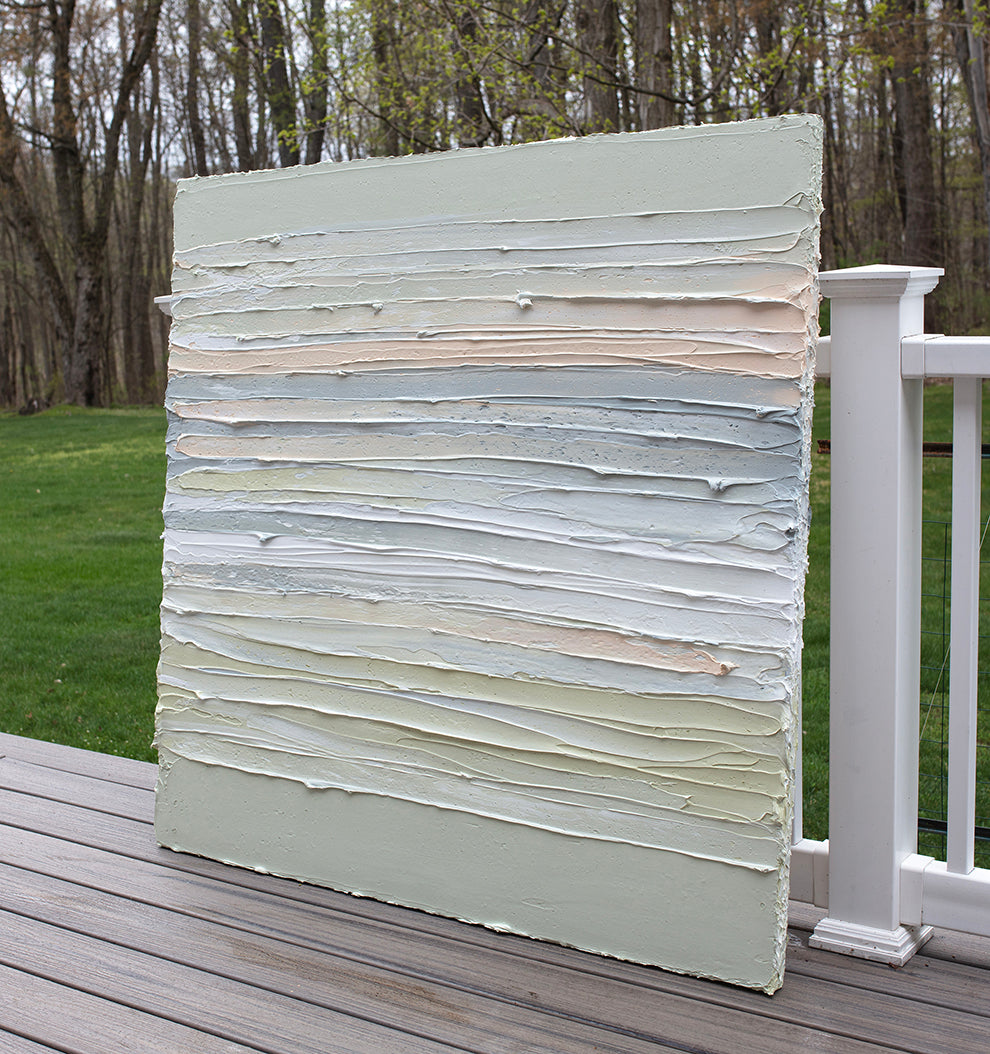 A peach, grey, white, celadon and sage green thickly textured painting leaning outside on a deck in natural light by Teodora Guererra.