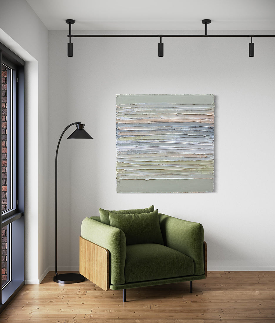 A peach, grey, white, celadon and sage green thickly textured painting by Teodora Guererra hanging on a white wall over a green chair with a black modern floor lamp to the left.